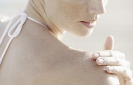 Žena nanosi kremu na svoje desno rame.